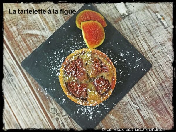 Tartelette à la figue entière sur une ardoise, quartiers de figue fraîche à côté