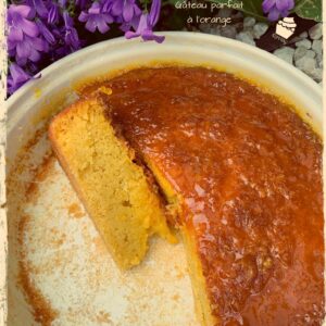 Gâteau à l’orange entamé et part dans le moule près de fleurs violettes