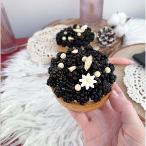 Tartelette mûres et vanille tenue à la main devant une autre tartelette